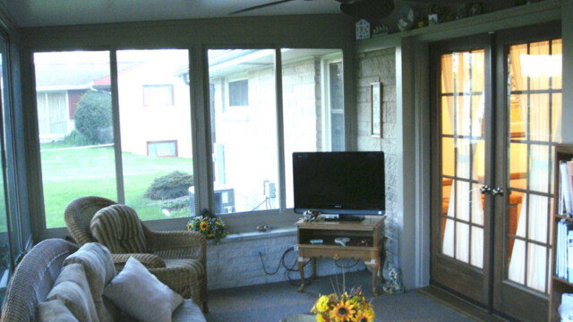 Cozy sunroom interior with wicker furniture, a sofa, and armchair arranged around a glass coffee table topped with sunflowers.