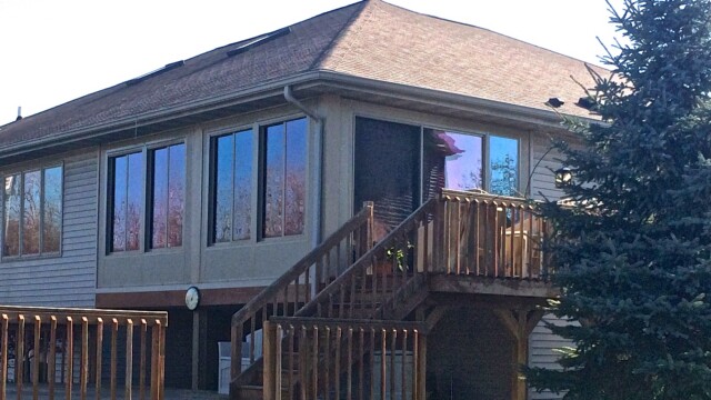 Elevated sunroom addition with large windows on the back of a two-story home, built above a wooden deck with stairs leading down.